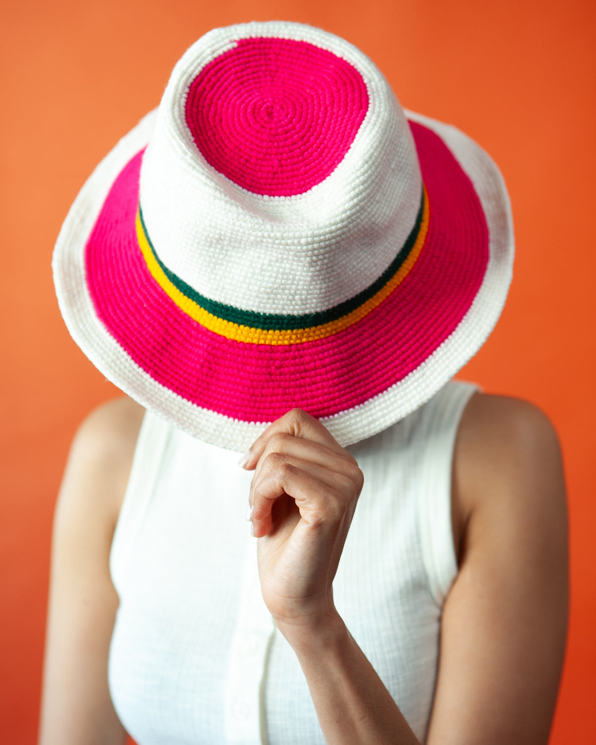 Woman wearing a pink and white Konso crochet fedora hat handmade in Ethiopia with green and yellow stripes and a wide brim.