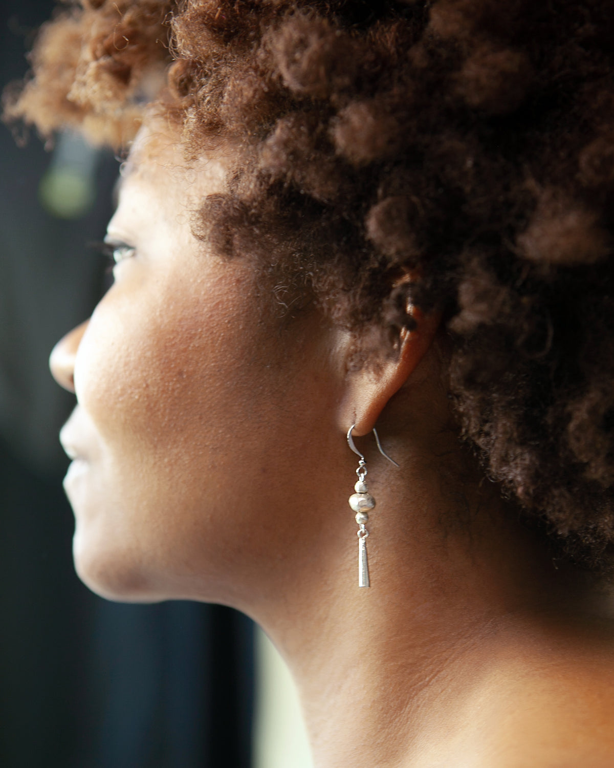 Model wearing silver-tone Ethiopian recycled brass bead and drop earrings handmade from repurposed metal.