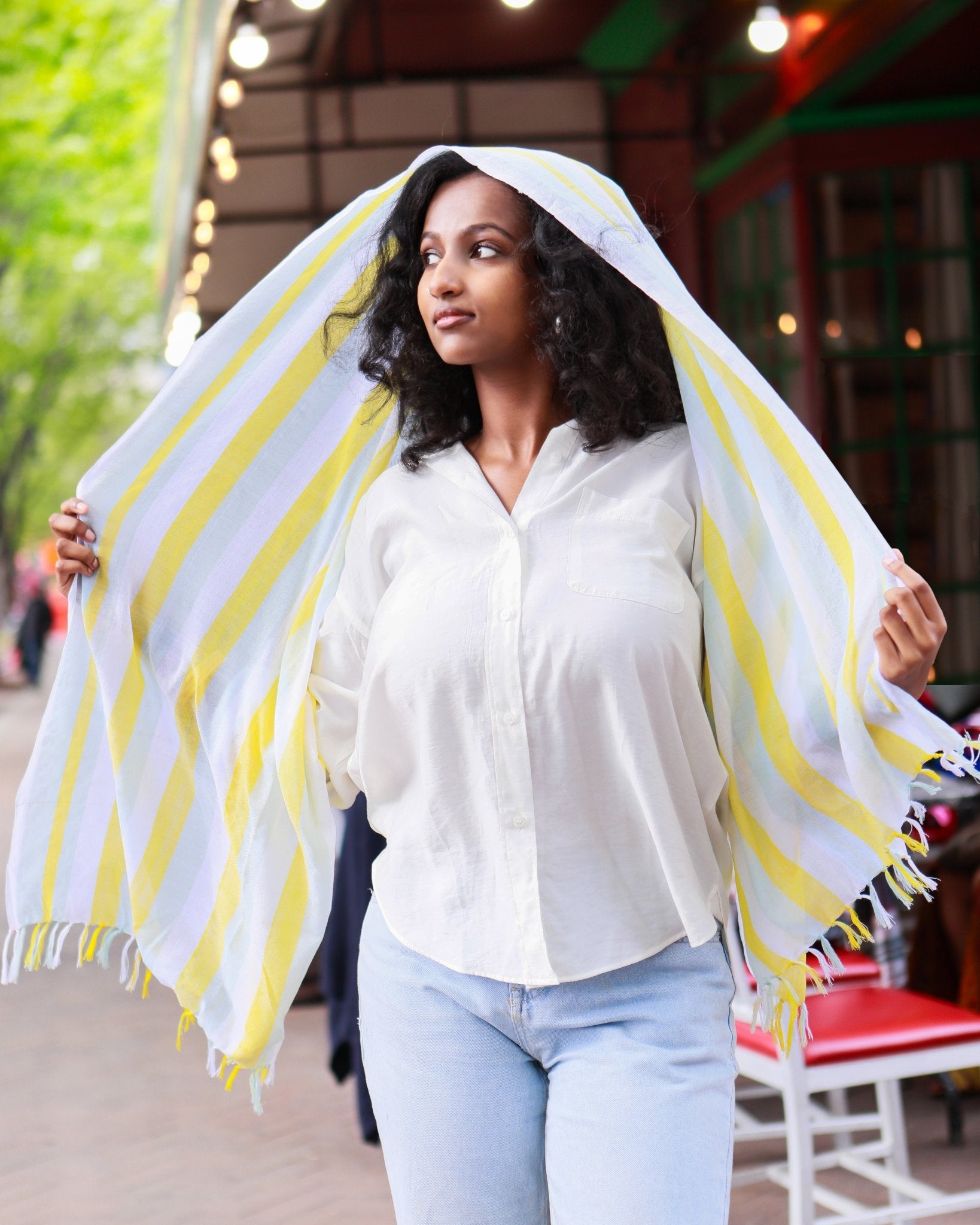 Woman wearing a handwoven yellow and white cotton scarf as a hooded shawl, headscarf, artisan-made in Ethiopia by Kelem